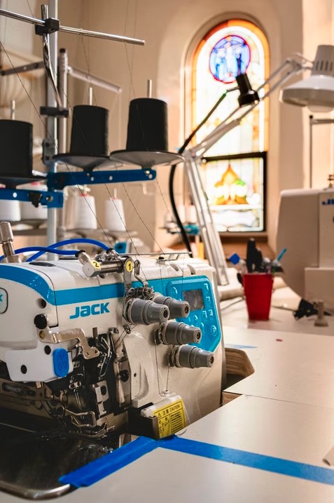A Jack industrial overlock serger with cones of thread, with a stained glass church window glowing behind it