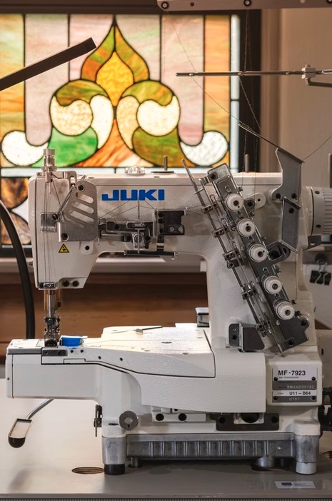 A Juki MF-7923 industrial coverstitch machine threaded and ready, framed by a stained glass window at HHGC