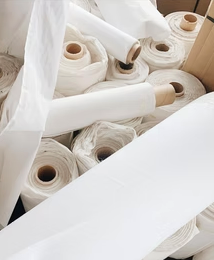 Rolls of white knit fabric stacked in the HHGC fabric room in Buchtel, Ohio