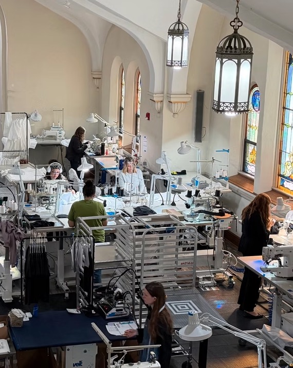 The HHGC production floor inside the former church, with sewists at industrial machines below tall arched and stained glass windows