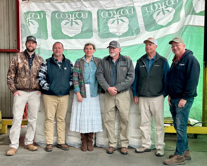 HHGC founder Betsy Franjola with American cotton supply chain partners standing in front of bales of U.S.-grown cotton